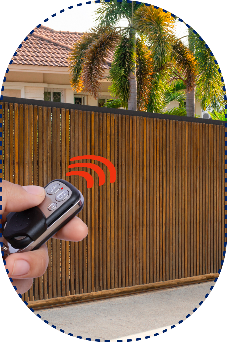 Hand holding a remote control with red signals in front of a wooden gate, with a house and palm trees behind.